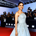 **

A professional photograph of Deepika Padukone, fully clothed in a modest, elegant gown, smiling confidently on a red carpet. The background shows flashing lights and cheering crowds. The image subtly suggests the fragrance Flowerbomb with floral accents in the background. Perfect anatomy, natural pose, appropriate attire, safe for work, high quality, professional.

**